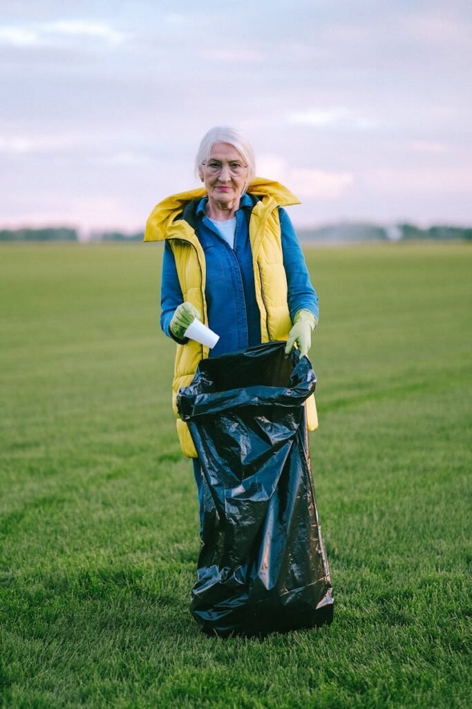 Senior woman cleaning up trash in a green field, promoting environmental care.