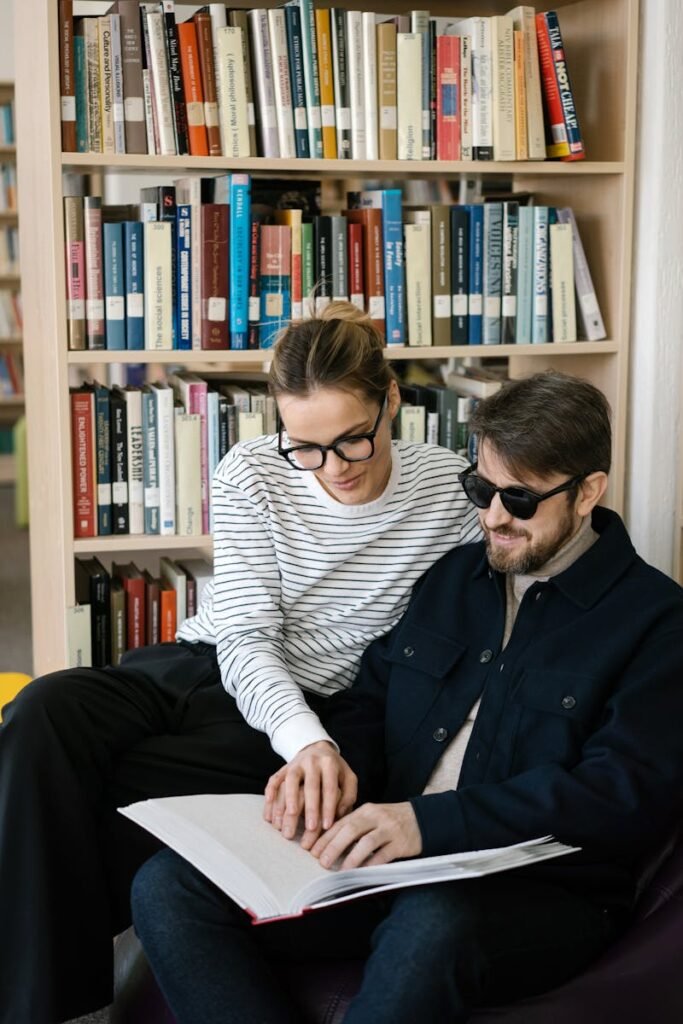 A man and woman reading a Braille book together in a library setting.